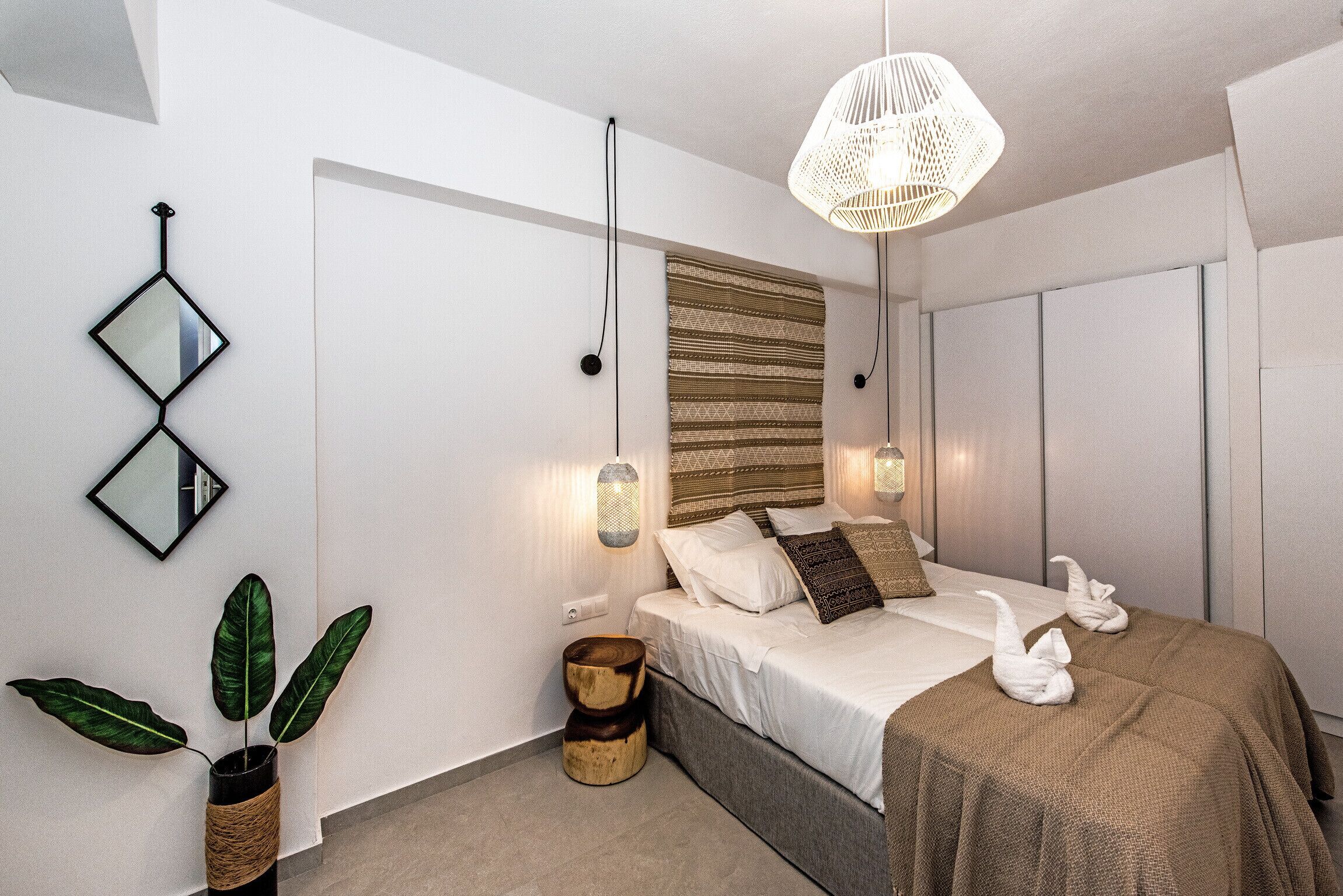 A modern bedroom with a bed, bedside lamps, a wall-mounted mirror, and a potted plant.