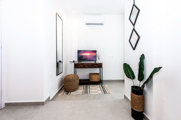 A hallway with a flat-screen TV on a wooden console, a woven pouf, a woven basket, and a potted plant. - Memoria villa,Private pool,Near amenities,Rethymno (Gerani)