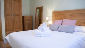 Un lit bien fait, avec du linge de lit blanc et une pile de serviettes pliées, une armoire en bois et un miroir au mur.
