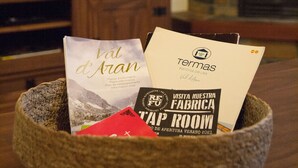 Un bol en pierre est posé sur une table en bois, à côté de quelques brochures et d’un livre. On aperçoit, au fond, un téléviseur à écran plat et une cheminée.
