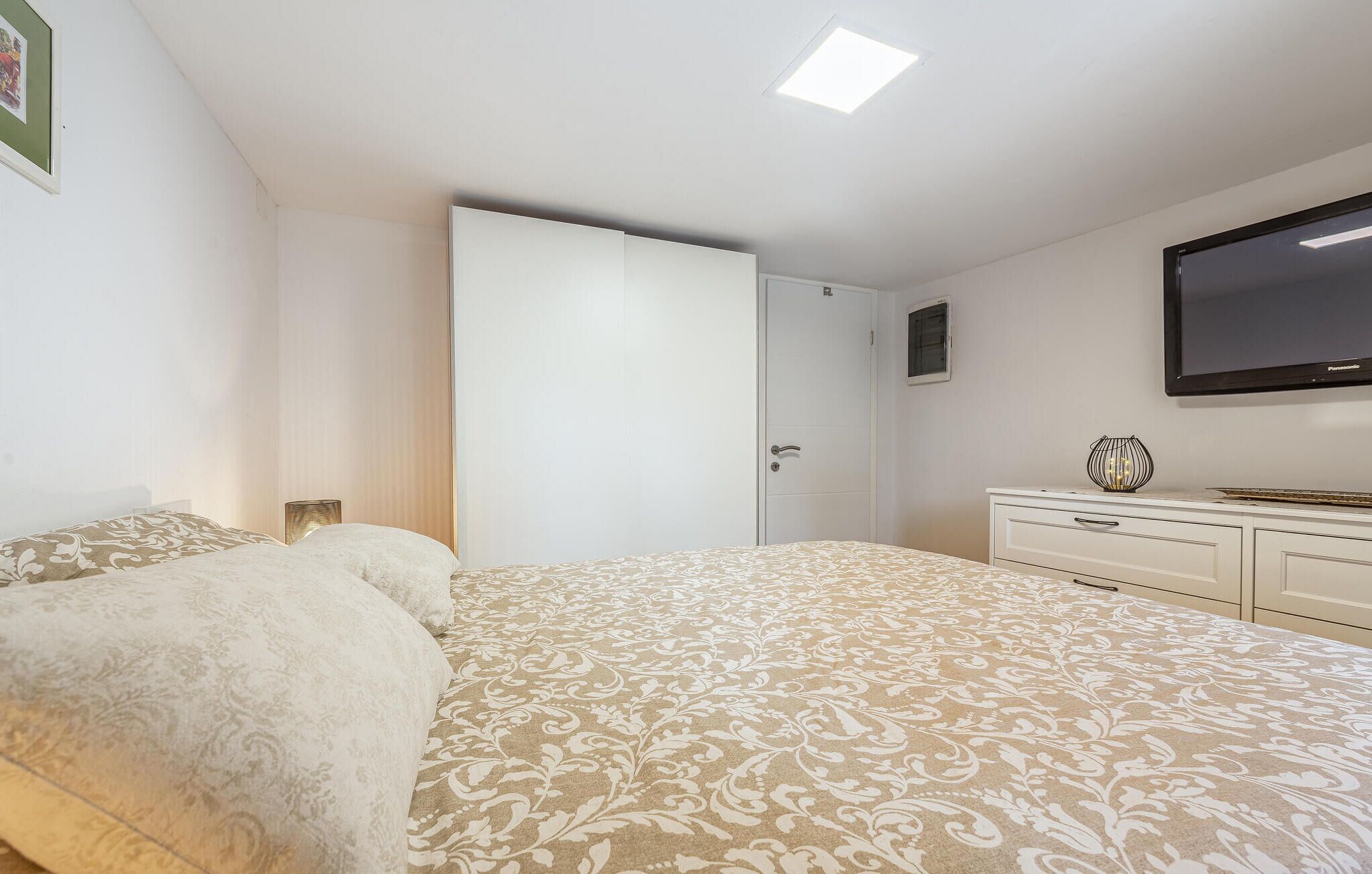 Een slaapkamer met een bed, een kast, een televisie en een deur.