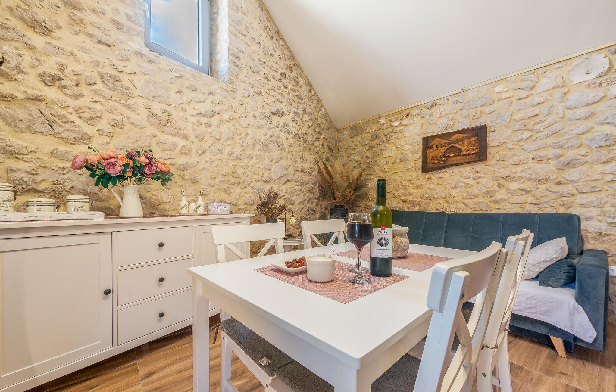 Un coin repas chaleureux avec un mur en pierre, une table blanche et un canapé bleu.