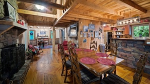 A wooden dining area with a stone fireplace, wooden ceiling beams, and a stone wall.