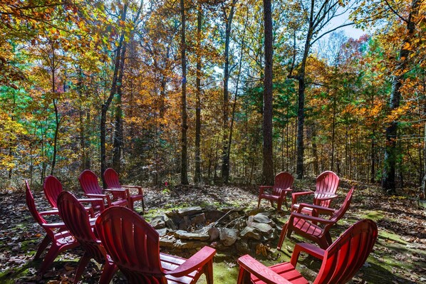 Een bos met een vuurplaats van steen en rode Adirondack-stoelen eromheen.