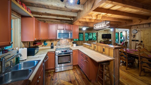 A rustic kitchen with wooden beams, a central island, stainless steel appliances, and a dining area with wooden furniture.