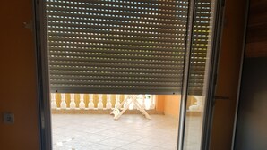 Une chambre avec un lit, une fenêtre avec des stores et une vue sur un balcon extérieur.