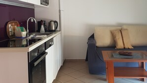 Une cuisine compacte équipée d’un four à micro-ondes, d’une bouilloire et d’une machine à café, d’un canapé avec des coussins et d’une petite table en bois.