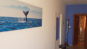 Un couloir orné d’un grand tableau représentant la queue d’une baleine, avec une porte bleue, un porte-manteau et une poubelle.