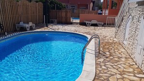 Une piscine dont le fond est recouvert de carreaux de pierre, entourée d’une clôture en bois et d’un mur de pierre.