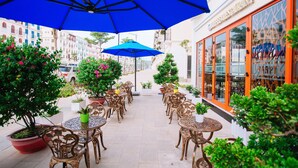 Un patio al aire libre con mesas y sillas, plantas en macetas y un paraguas azul.
