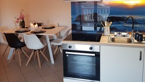 A modern kitchen with a built-in oven, a dining area with white chairs, and a wall-mounted light fixture.