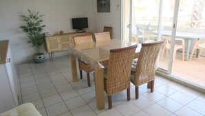 A dining area with a glass table and wicker chairs, a television on a wooden cabinet, and a potted plant. - Sol-y-Days le Mayflower, Apartment for 6 people with swimming pool (Le Grau-du-Roi)