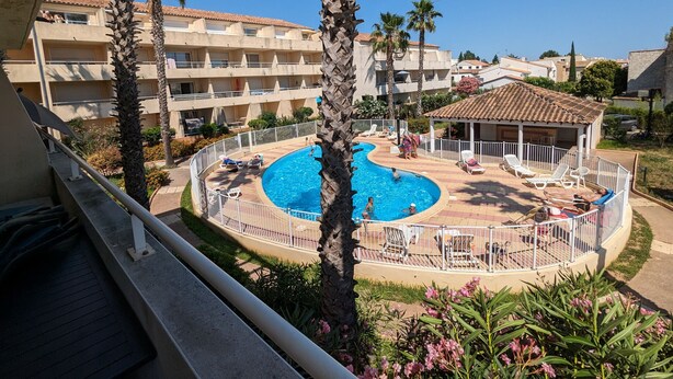 A swimming pool surrounded by lounge chairs and palm trees, with a building in the background. - Sol-y-Days le Mayflower, Apartment for 6 people with swimming pool (Le Grau-du-Roi)