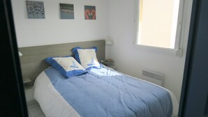 A neatly made bed with blue and white bedding, a bedside table with a lamp, and three wall art pieces above the bed. - Sol-y-Days le Mayflower, Apartment for 6 people with swimming pool (Le Grau-du-Roi)