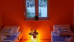 Une petite pièce avec deux lits simples, une petite table sur laquelle est posée une bougie, et une fenêtre.
