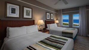 A hotel room with two beds, a ceiling fan, framed pictures on the wall, and a view of the ocean through large windows. - Oceanfront Villa at Grand Dunes (Myrtle Beach)