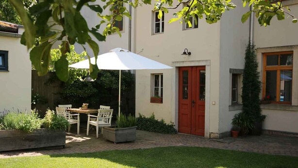 A patio with a table and chairs, a white umbrella, and a red door. - Stylishly furnished vacation apartment in Dresden including bicycles, close to the city center (Dresden)
