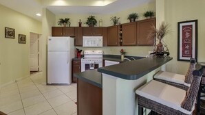 A compact kitchen with a refrigerator, stove, microwave, and a small dining area with a counter and two chairs. - Beautiful Condo with a Tree House Feel (Port St. Lucie)
