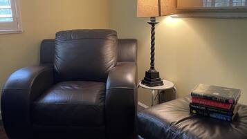 Ein Zimmer mit Ledersessel, einem kleinen Hocker, einer Lampe und einem Stapel Bücher auf dem Hocker.