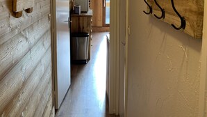 Un estrecho pasillo con paredes de madera, un área de cocina al fondo y una puerta que da a otra habitación.
