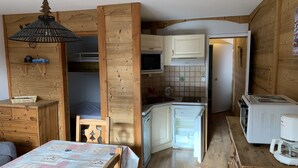 Una cocina compacta con armarios de madera, microondas, refrigerador y cafetera.