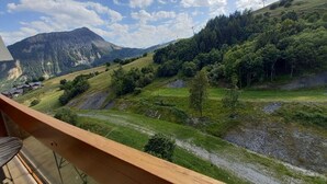 Paisaje montañoso con cielo despejado y un balcón de madera con vistas al valle.