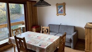 Un comedor con una mesa cubierta por un mantel estampado, sillas de madera, un sofá gris y un mueble de madera.