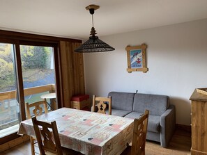 Ein Essbereich mit einem Tisch, der mit einer gemusterten Tischdecke bedeckt ist, Holzstühle, ein graues Sofa und ein Holzschrank.
