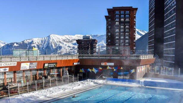 Una piscina con carriles, un edificio con un telesilla y montañas nevadas al fondo.