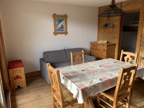 A cozy room with a wooden dining table, chairs, a grey sofa, and a wooden cabinet.