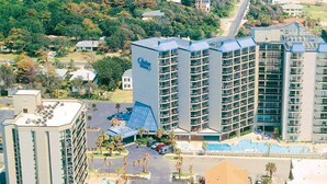 Un hotel de gran altura con varios balcones, piscina y una zona ajardinada con palmeras.