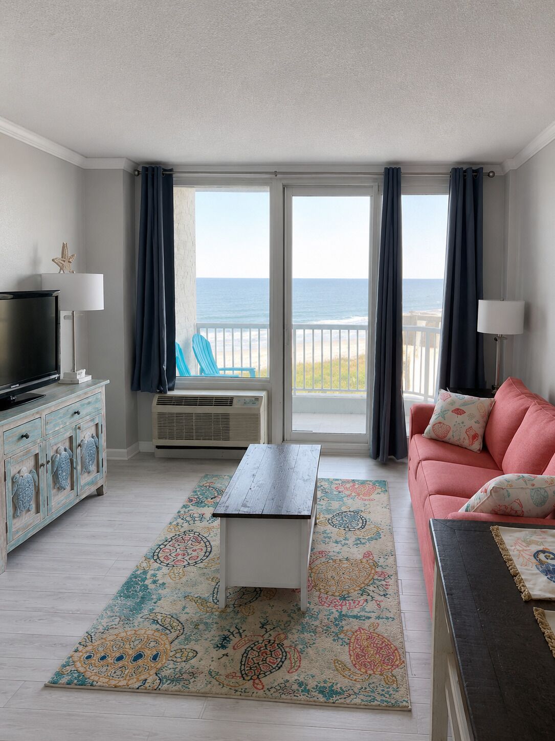 A living room with a television, a sofa, a coffee table, and a view of the beach.
