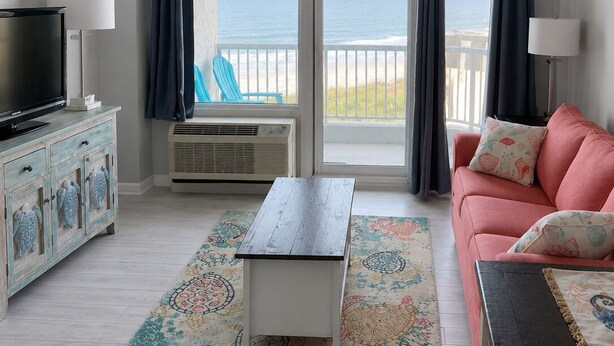 Una sala de estar con televisor, sofá, mesa de centro y vista a la playa.