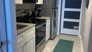 Una cocina moderna con armarios blancos, un microondas negro, electrodomésticos de acero inoxidable y una alfombra verde.