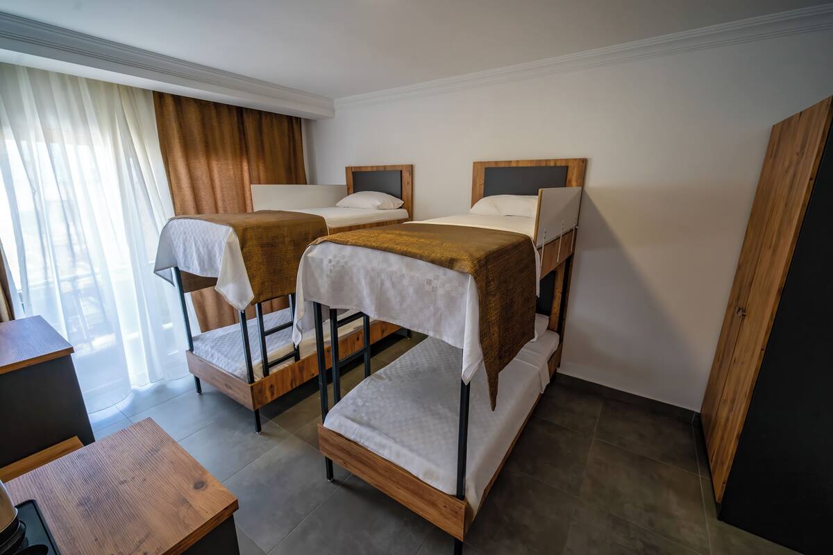 Een kamer met drie stapelbedden, een houten bureau en een raam met gordijnen.