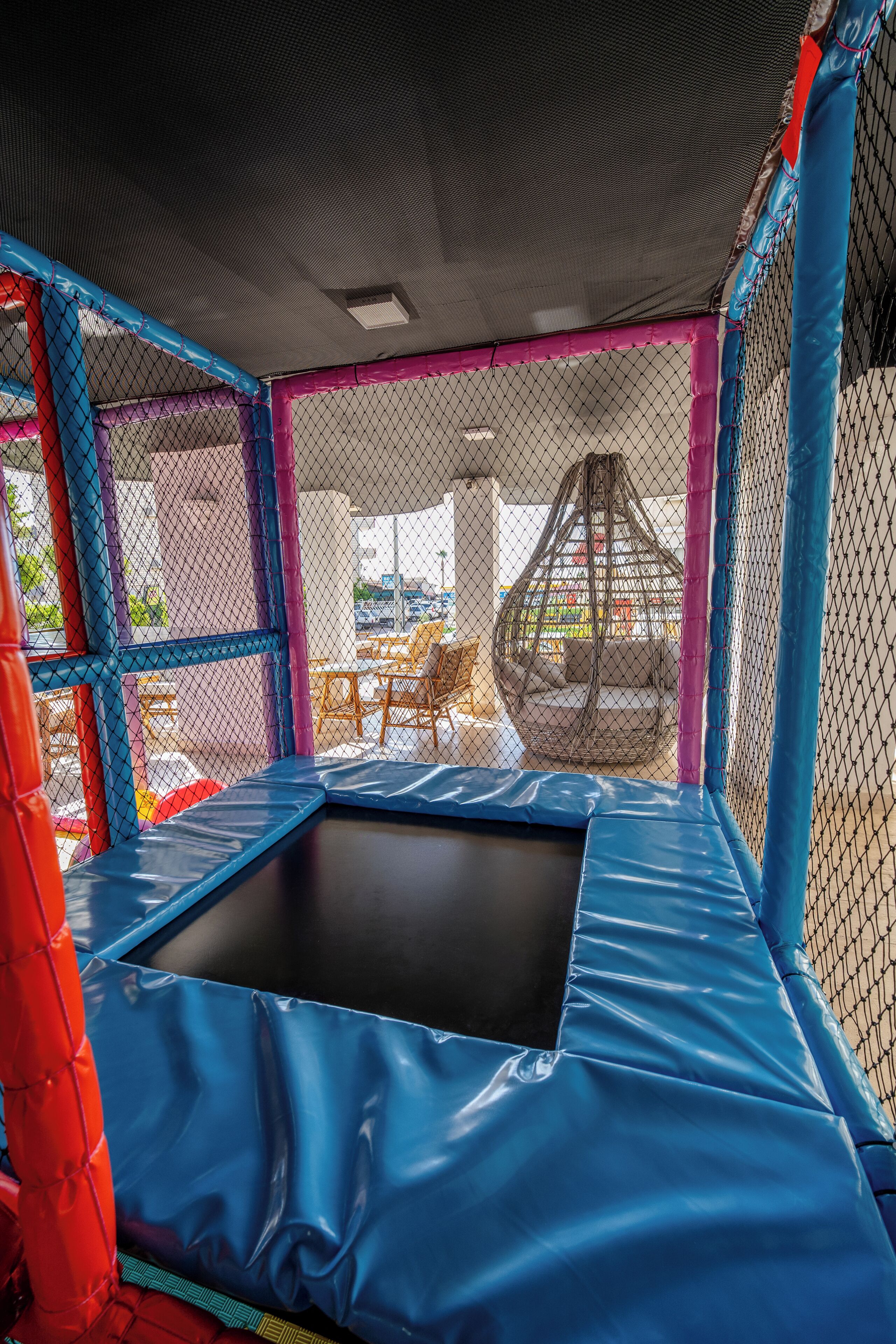 A trampoline with a safety net enclosure, a hanging swing, and a view of an outdoor patio area.