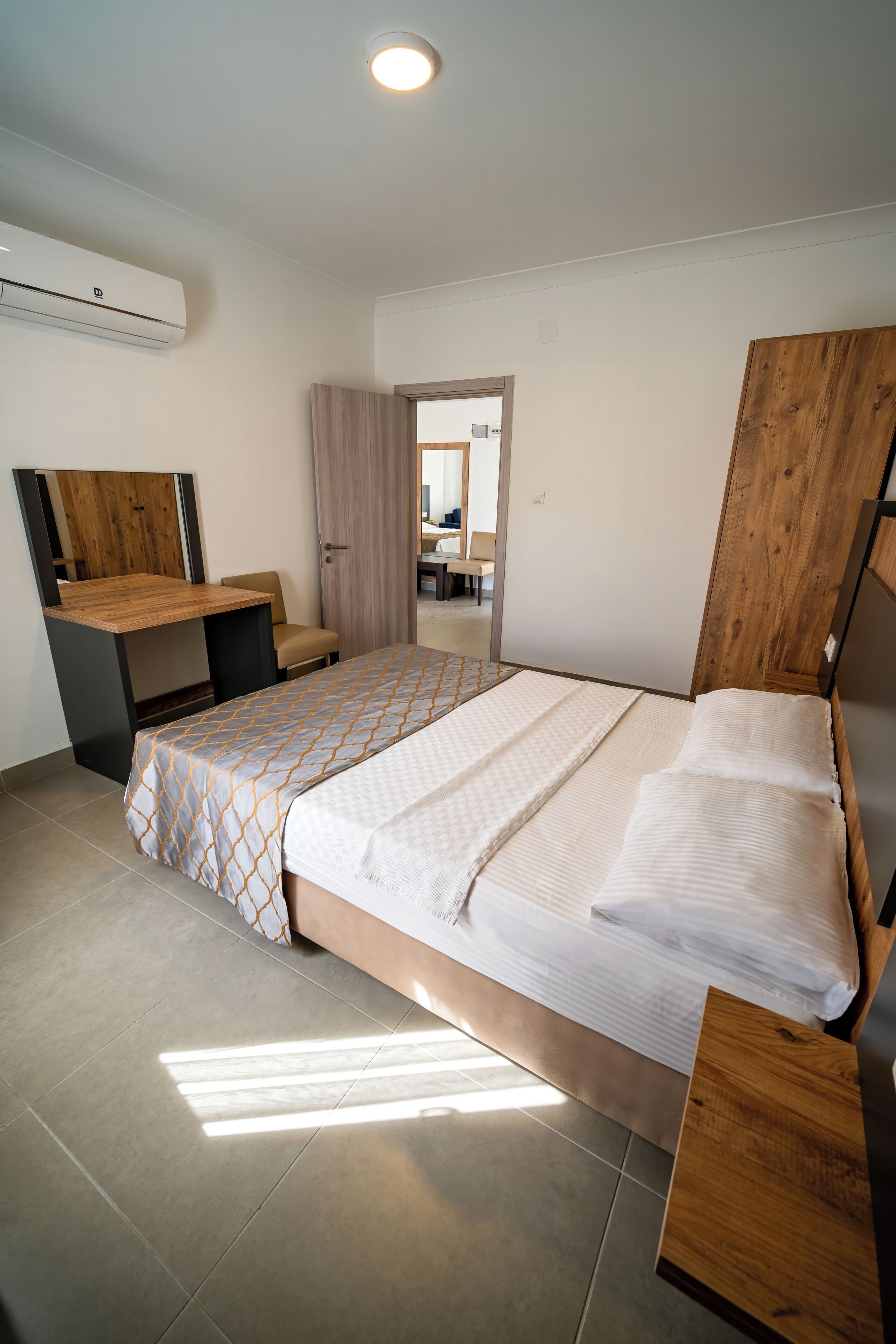 A bedroom with a bed, a desk, a chair, and a mirror.