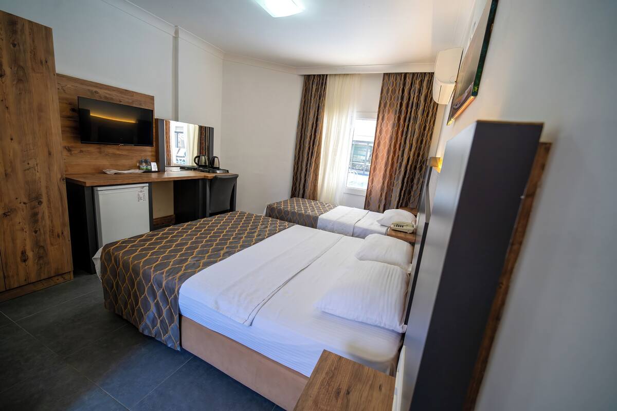 Een hotelkamer met een bed, een bureau met een televisie, een kleine koelkast en een raam met gordijnen.