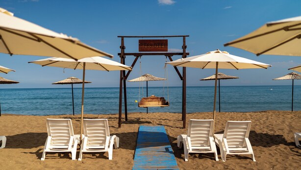 A beach with white lounge chairs, a wooden walkway, and umbrellas. - Club Efes Otel (Silifke)