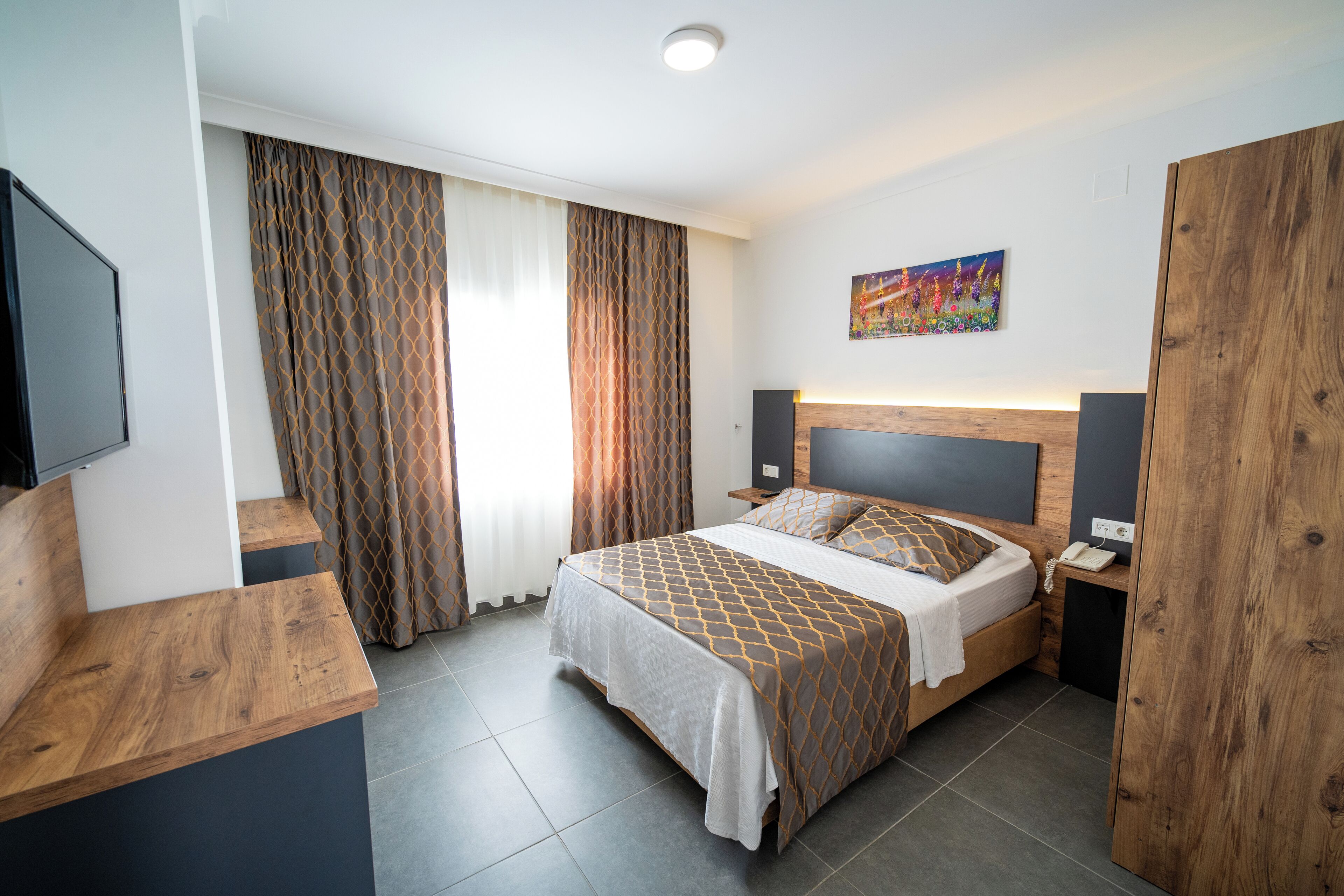 Ein modernes Hotelzimmer mit einem Bett, Nachttischen aus Holz, einem Flachbildfernseher und einem Bild an der Wand.