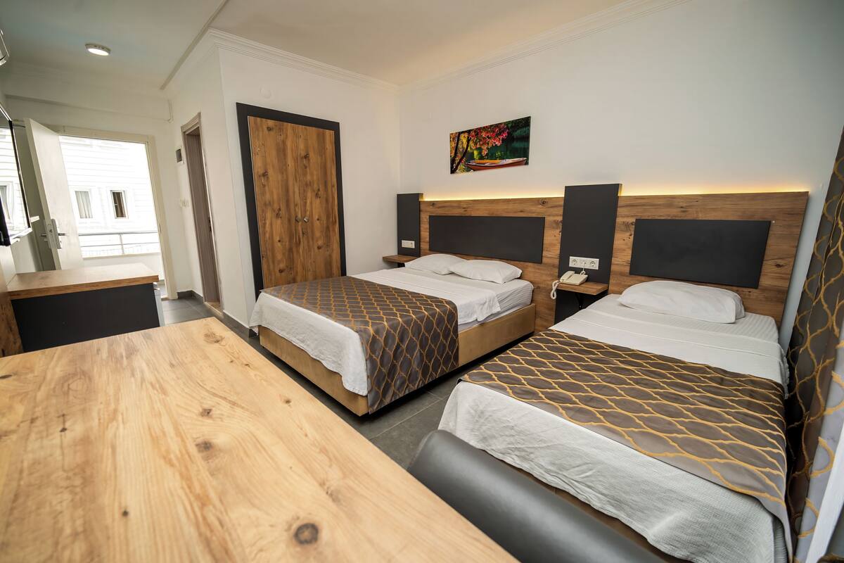 Een hotelkamer met twee bedden, een houten tafel, een schilderij aan de muur en een deur die leidt naar een balkon.