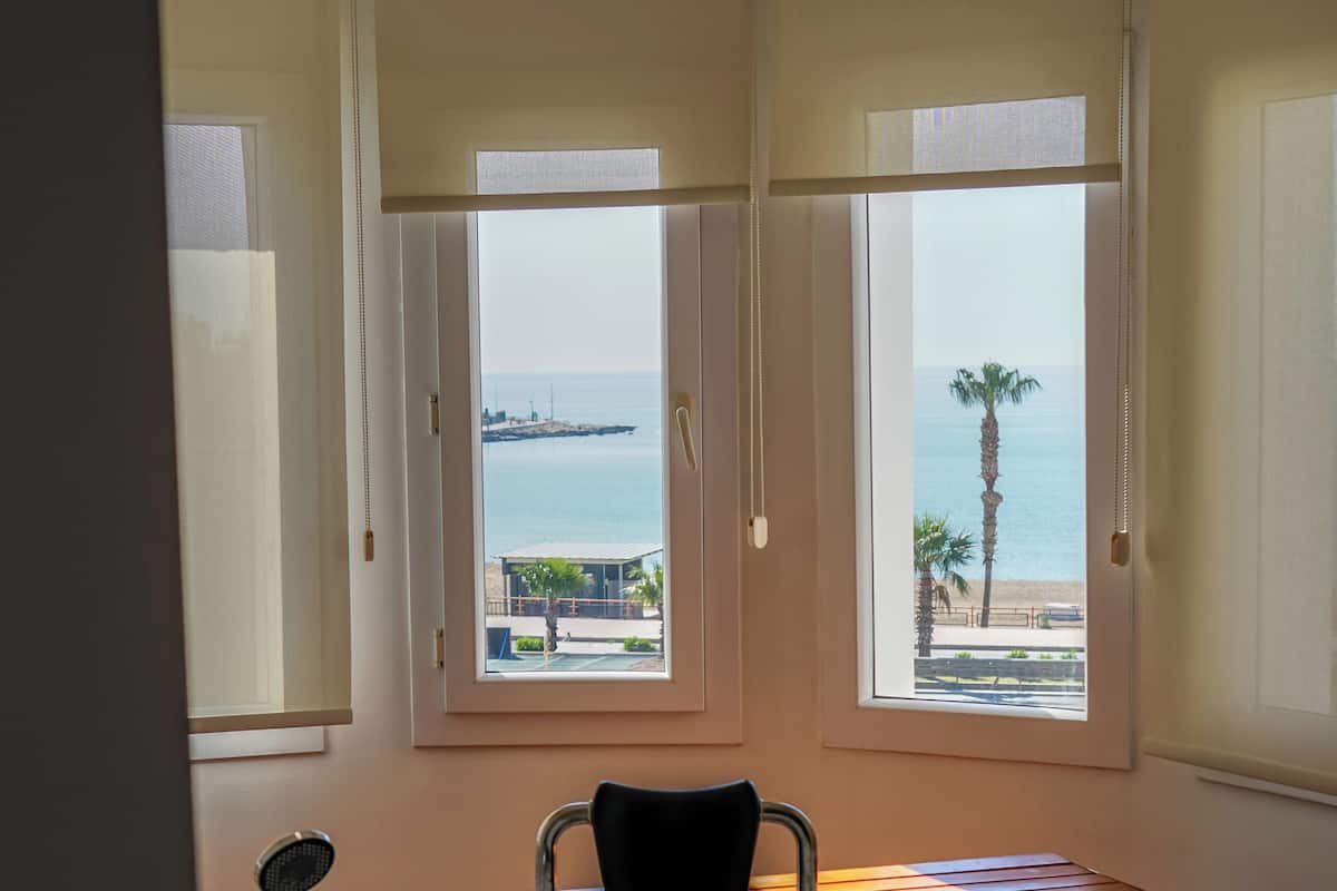 Een badkamer met een bad, houten vloer en grote ramen met uitzicht op zee.