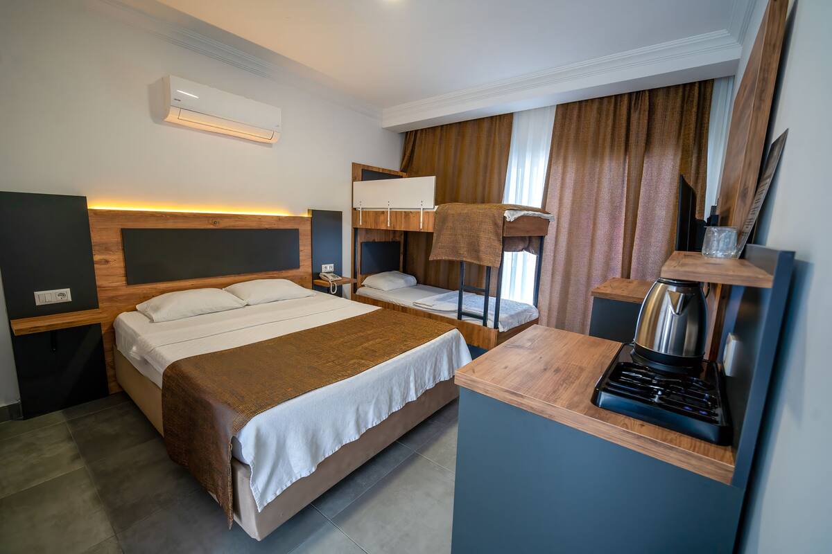 Een hotelkamer met een stapelbed, een bureau met een waterkoker en een wandairconditioner.