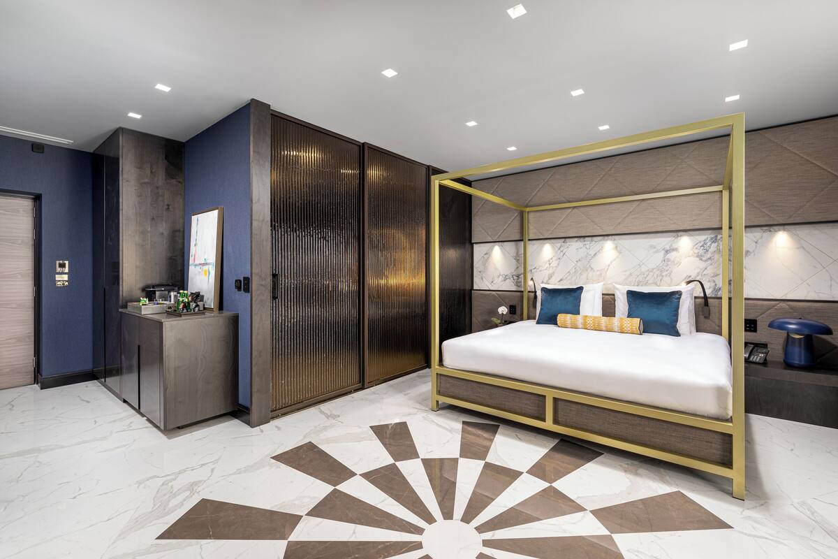 A modern bedroom with a four-poster bed, a desk, and a wardrobe.