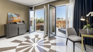 Una habitación de hotel moderna con un gran ventanal corredero que da a un balcón, un área de comedor con mesa y sillas, y un cuadro decorativo en la pared.