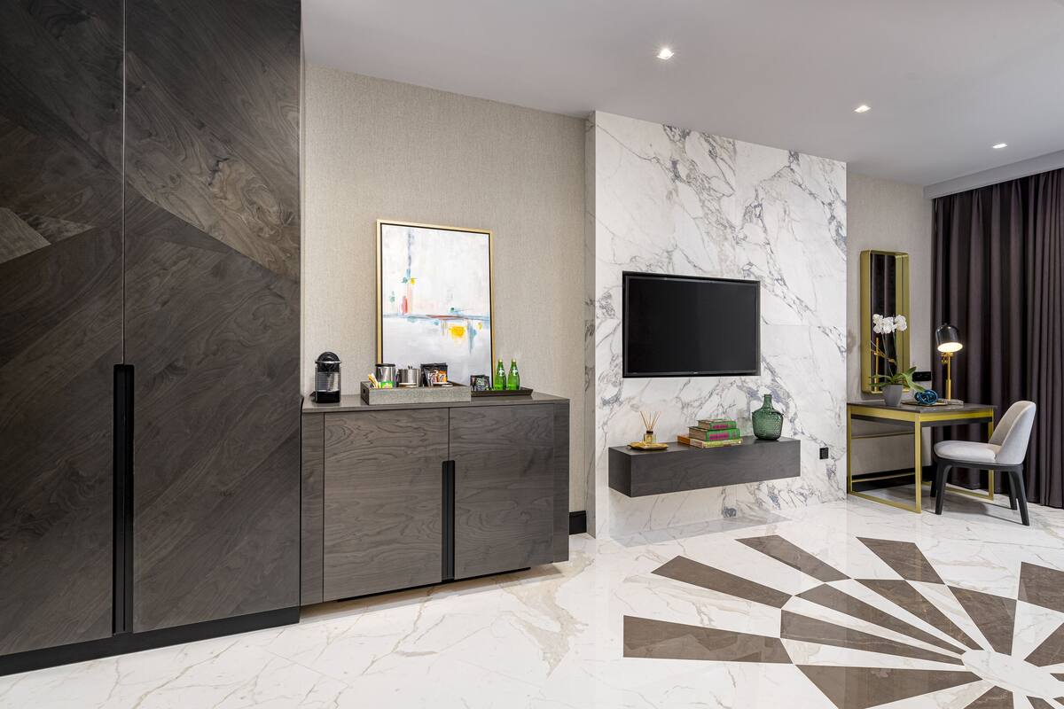 A modern living room with a marble floor, a flat-screen TV mounted on the wall, a dark wood cabinet, and a desk with a chair.