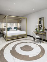 Ein modernes Schlafzimmer mit einem Himmelbett, einem Schreibtisch mit Stuhl, einem großen Spiegel und einem dekorativen Teppich.