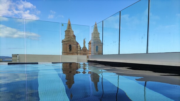 Piscina azul cristalina con reflejos de una iglesia y una estatua.