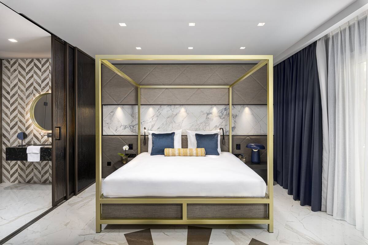 A modern bedroom with a four-poster bed, marble walls, and a herringbone-patterned wallpaper.