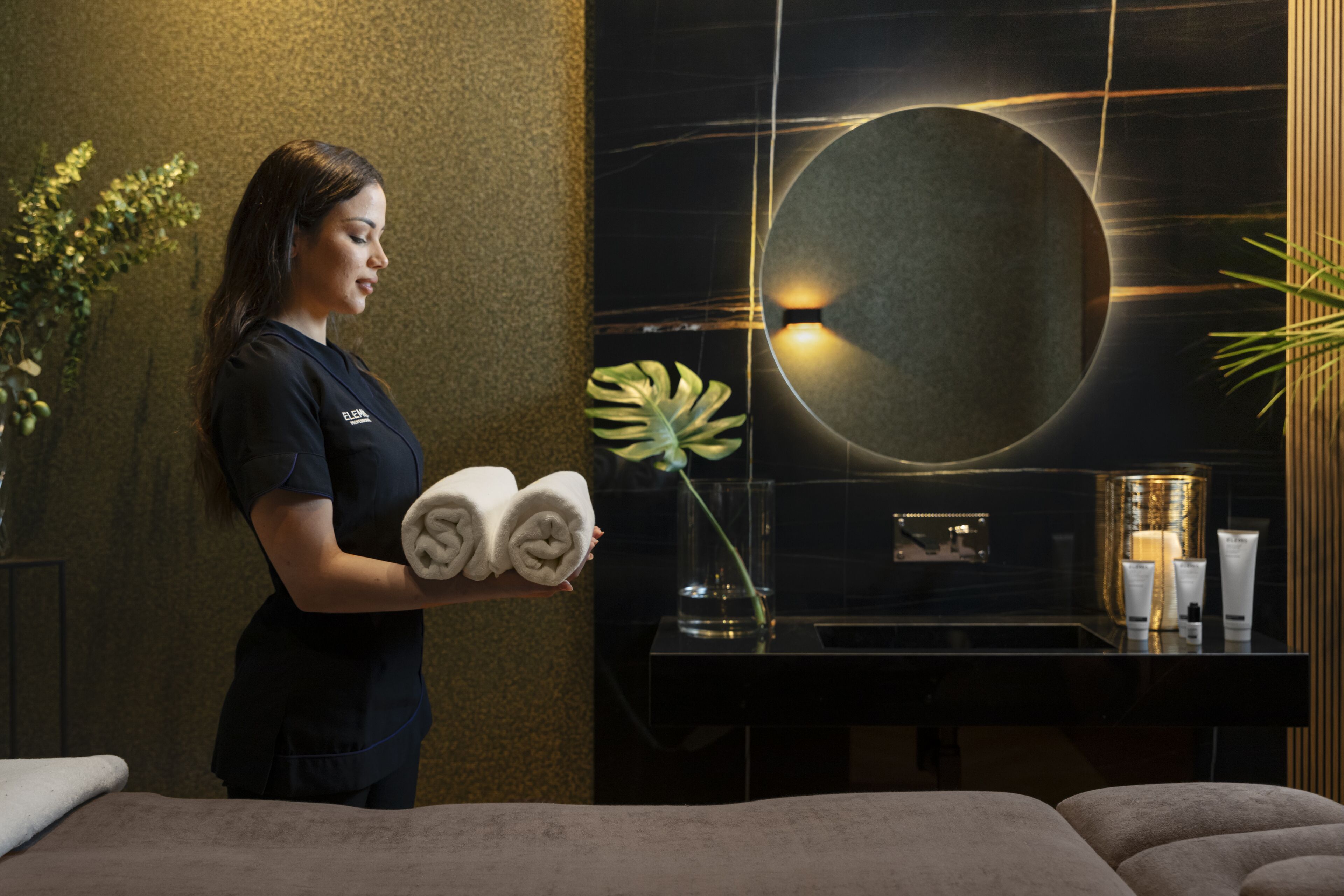 A hotel room with a large bed, a small table with toiletries, a mirror, and a plant.